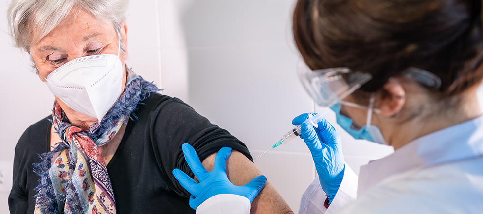 Mevrouw op leeftijd krijgt een prik in de bovenarm.